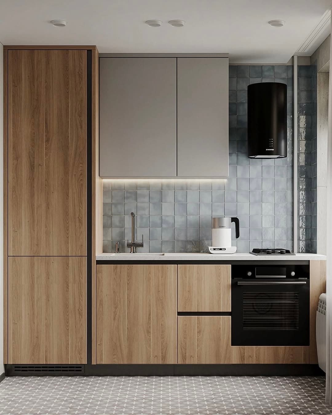 Modern kitchen with light wood and taupe cabinets, pale blue square tile backsplash, black cylindrical range hood, built-in oven, white countertops, and patterned tile flooring.