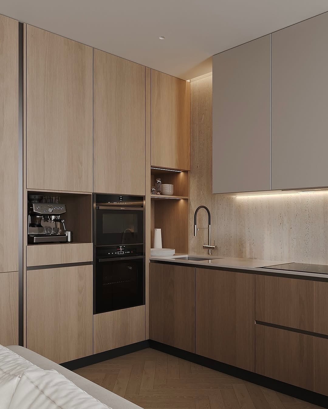 Contemporary L-shaped kitchen with light wood grain cabinets, built-in espresso machine, stacked black ovens, and white quartz countertops with textured beige backsplash. Integrated LED lighting throughout with herringbone wood flooring
